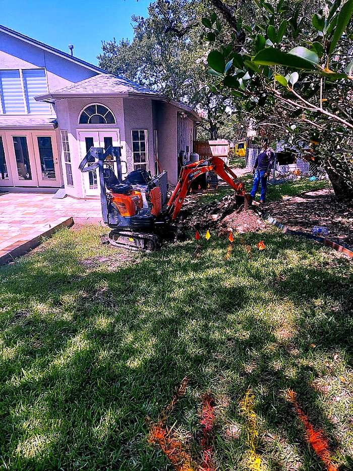 Mini excavator digging for underground plumbing access in a Boerne backyard