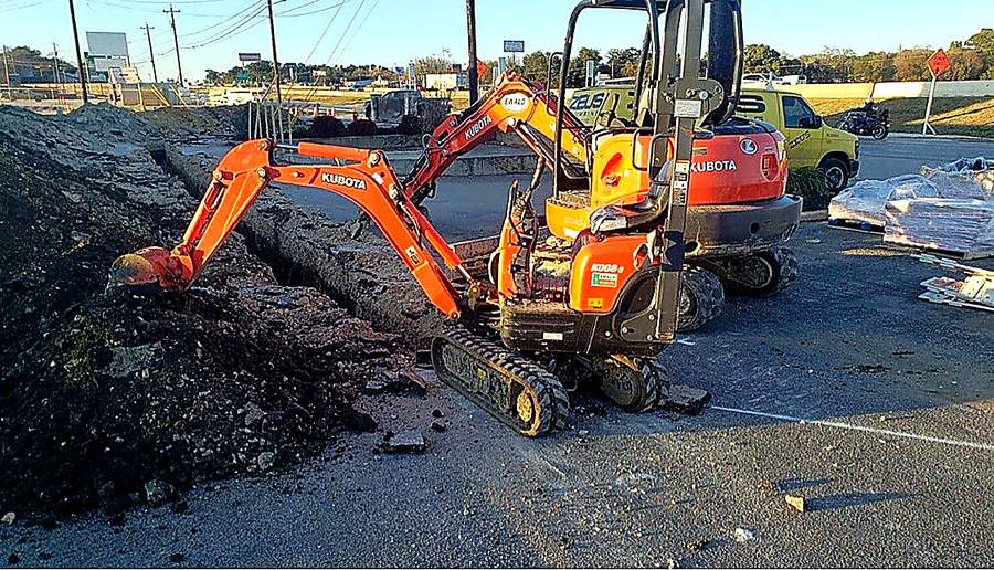 Kubota mini excavator trenching at a Zeus Plumbing job site with a yellow Zeus service van nearby