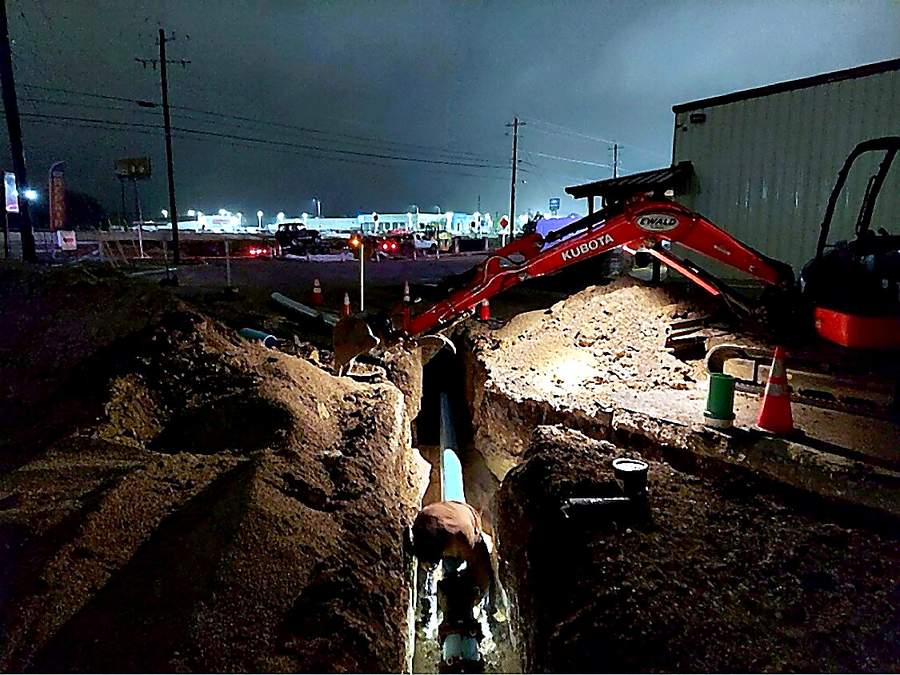 Night sewer pipe installation in a deep trench by a San Antonio plumbing crew