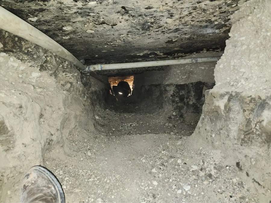 Excavated plumbing tunnel beneath a concrete slab with drain piping visible overhead