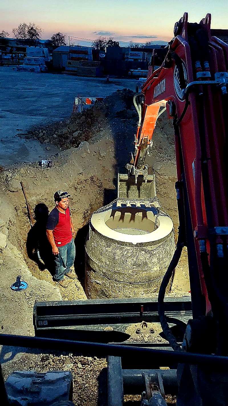 Excavator setting a concrete tank for underground utility work near San Antonio