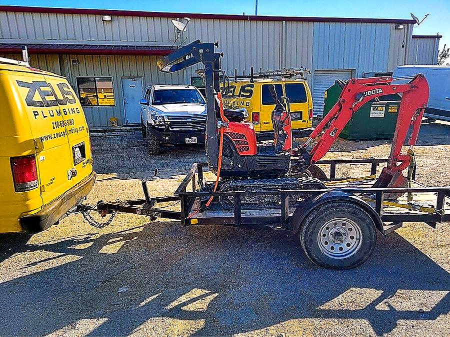 Zeus Plumbing van towing a Kubota excavator to a job site near San Antonio